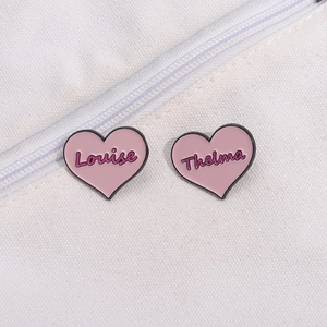 Pink heart enamel brooches with Louise and Thelma names on white canvas fabric background
