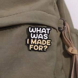 Detail of What Was I Made For enamel pin attached to a green canvas backpack
