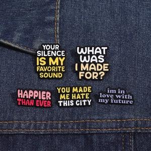 Close-up of five black enamel inspirational lyric pins on a denim fabric background