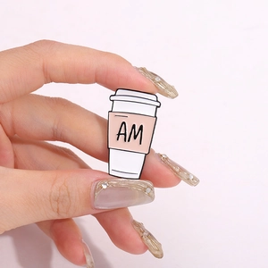 Minimalistische Emaille-Anstecknadel in Kaffeetassenform mit AM-Schriftzug in der Hand