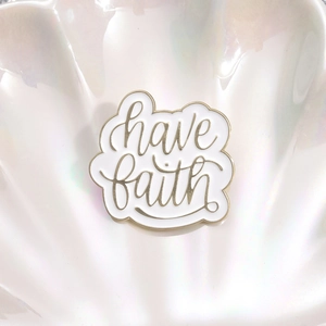 Irregular enamel brooch with gold have faith script on white background in shell tray
