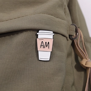 Makroaufnahme einer Emaille-Kaffeetassen-Anstecknadel mit AM-Buchstaben auf einer Tasche