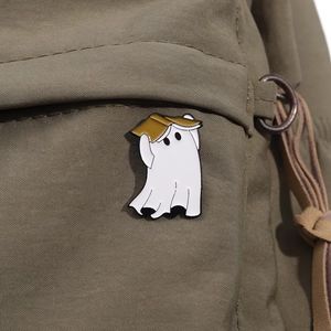 Close-up of white ghost enamel pin with gold hat on olive green canvas fabric texture