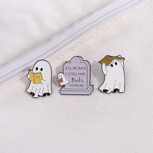 Detailed view of three cute enamel ghost pins with books on a white canvas texture