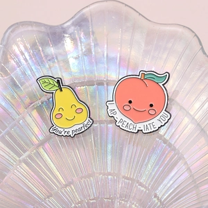 Cartoon pear and peach enamel pins with cute expressions on a pearl shell tray