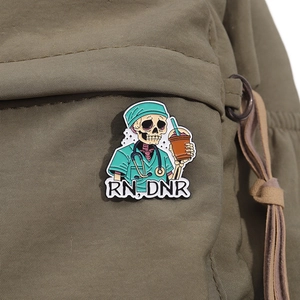 Detail of RN DNR enamel pin featuring a skeleton nurse with iced coffee on green fabric