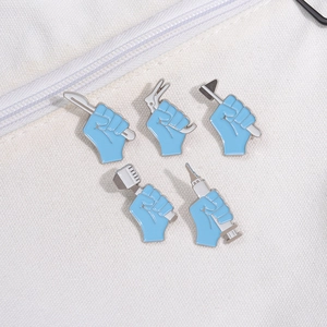 Set of 5 medical enamel pins with blue hand holding surgical tools on a canvas bag