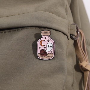 Detail of Halloween enamel pin with ghost and potion bottle on green canvas fabric
