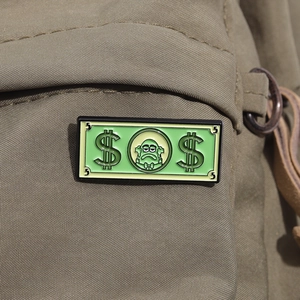 Detail of creative green banknote enamel pin with cartoon character on a canvas backpack