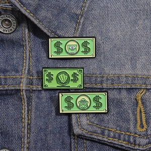 Funny green money enamel pins with cartoon characters on a blue denim jacket pocket