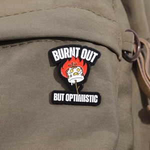 Funny burnt marshmallow enamel pin with Burnt Out But Optimistic text on canvas bag