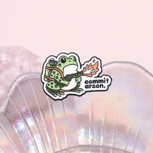 Detail of green enamel frog pin with flamethrower and humorous commit arson text
