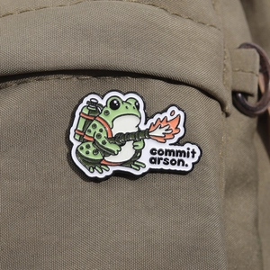 Vue détaillée de l'épingle en émail grenouille pyromane avec lance-flammes sur toile