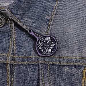 Détail du pin's émaillé en forme de poêle avec texte sur col de veste en jean