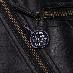 Détail d'un pin's en émail violet en forme de poêle avec texte d'humour sur cuir noir
