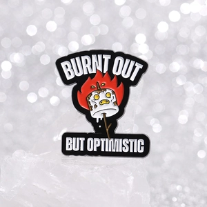 Funny enamel pin featuring a burnt marshmallow and Burnt Out But Optimistic text
