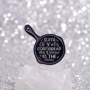 Purple skillet enamel pin featuring humorous cornbread quote on white crystal background
