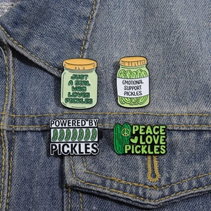 Set of four fun green pickle enamel pins attached to a blue denim jacket pocket