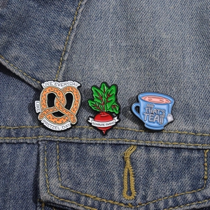 Détail de pin's émaillés Pretzel Day, Schrute Farms et tasse de thé sur tissu denim