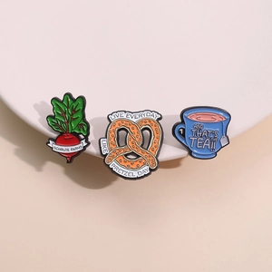 Lot de 3 broches émaillées motif betterave, bretzel et tasse à thé sur plateau blanc