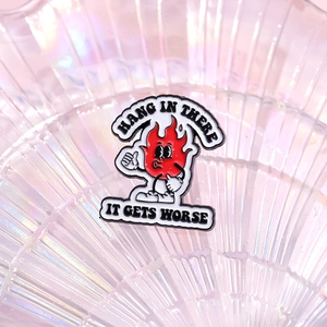 Cartoon red flame enamel pin with Hang In There text on a textured glass background