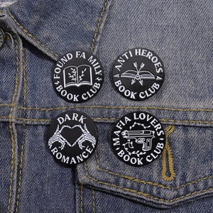 Detail of four black and white enamel badges featuring book themes on denim jacket