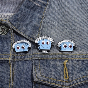 Detailed view of three blue toaster enamel pins with funny quotes on denim jacket fabric