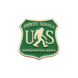 Bigfoot Forest Service enamel pin featuring a green shield design with gold metal edges