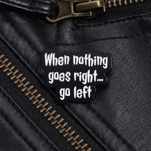 Close-up of black enamel pin with Go Left slogan on a black leather jacket texture