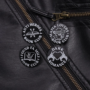 Detail of four dark romance enamel pins featuring books and pistols on a black leather jacket