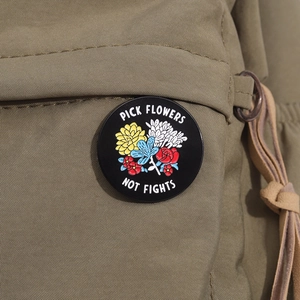 Detail view of Pick Flowers Not Fights round enamel pin on a green canvas backpack