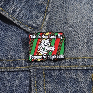 Cartoon zebra enamel pin with humor quote on blue denim jacket, colorful striped design