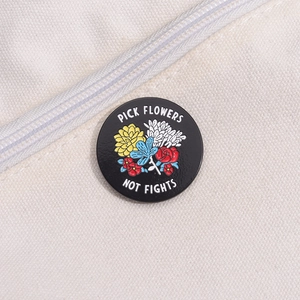 Detail view of round enamel pin with flowers and Pick Flowers Not Fights text