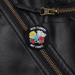 Detail of floral enamel pin with Pick Flowers Not Fights slogan on black leather jacket