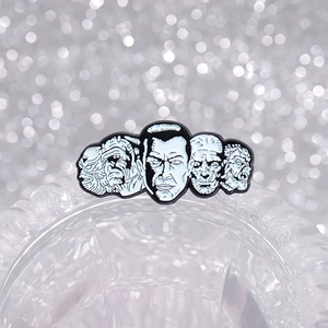 Five classic horror movie monster enamel pins in black and white finish on a stand