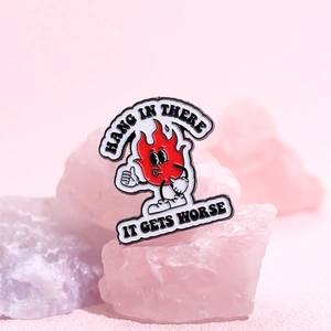 Enamel pin with a red cartoon flame giving a thumbs up and motivational text design