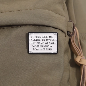 Detail of creative enamel pin on green canvas showing funny team meeting quote text