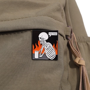 Detail of I'M FINE enamel pin with flaming skeleton design on green canvas bag