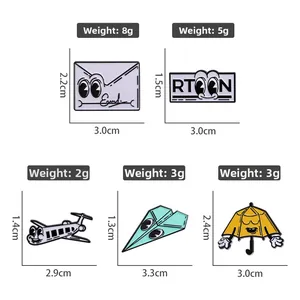 Detailed view of five cartoon enamel pins including paper plane, envelope, and umbrella shapes