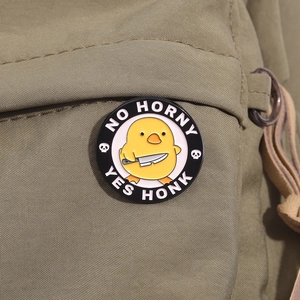 Close-up of a cartoon yellow duck enamel pin with a knife on green canvas bag