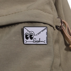 Détail macro du pin's émaillé enveloppe cartoon sur un fond en nylon vert