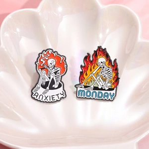 Punk style skull enamel pins with burning flames and Anxiety Monday text on pink background