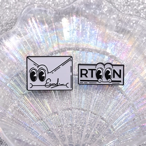 Cartoon envelope and letter enamel brooch set displayed on a shimmering shell tray
