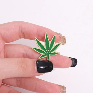 Hand holding a green enamel leaf brooch with gold edges in a minimalist white setting
