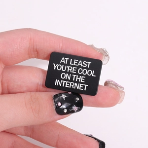 Minimalist enamel pin featuring white AT LEAST YOU'RE COOL ON THE INTERNET text on black