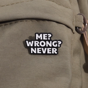 Badge en émail noir avec texte « ME? WRONG? NEVER » épinglé sur un sac en toile