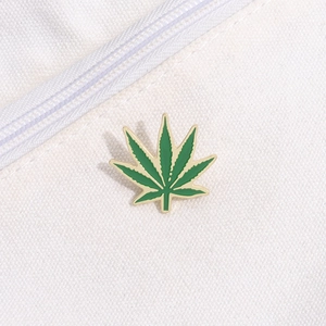 Macro detail of green enamel hemp leaf pin with gold plating on white canvas