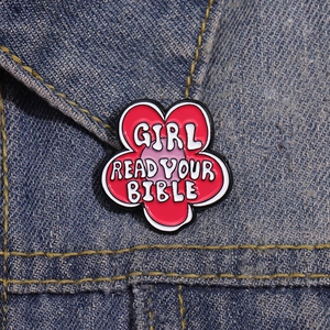 Close-up of a red flower enamel brooch with 'Girl Read Your Bible' on a denim jacket