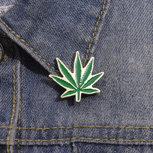 Macro detail of a green enamel leaf brooch pinned on a blue denim jacket collar