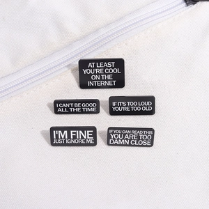Detail of five black rectangular pins with witty English slogans on a white canvas bag